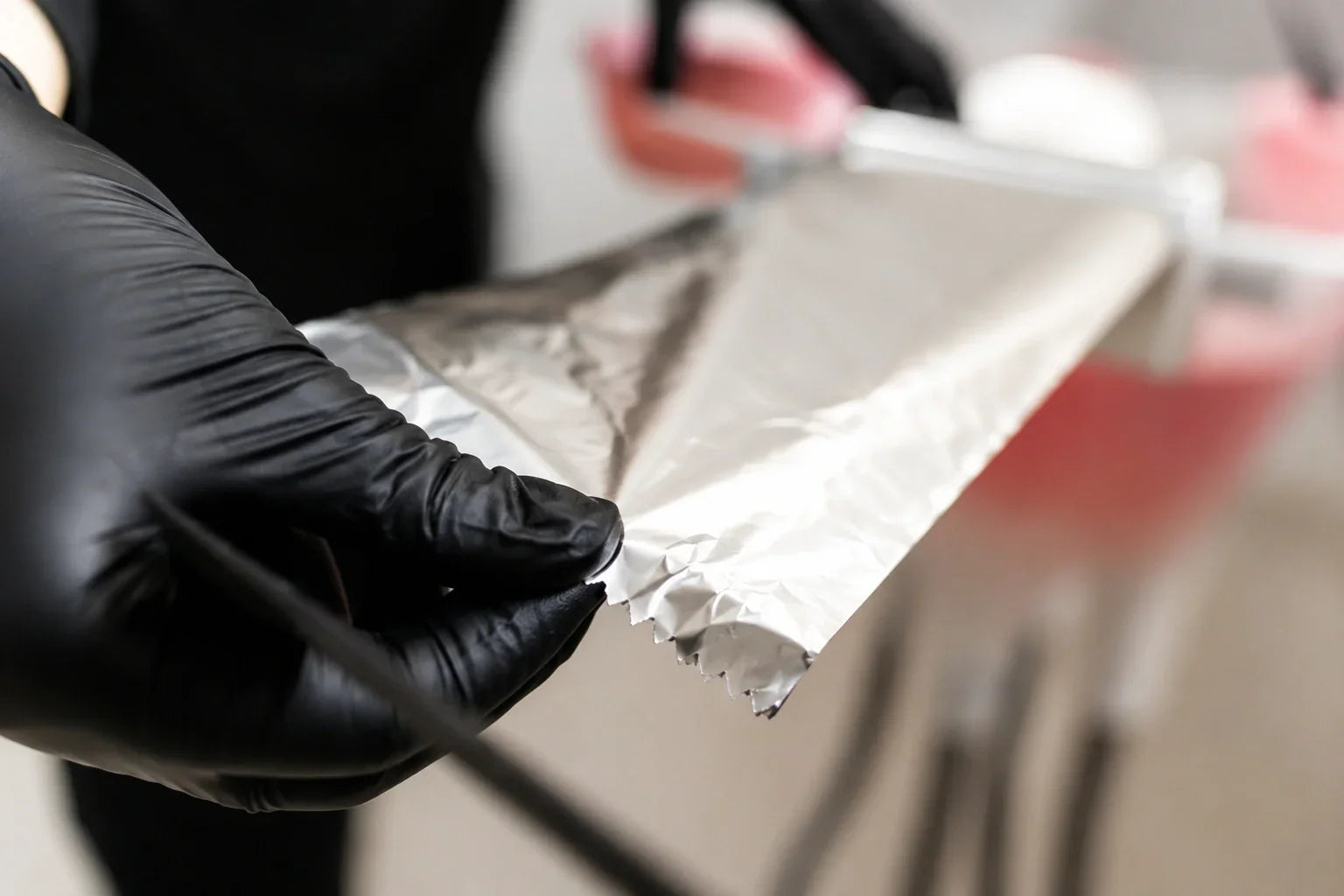 Professional hairstylist holding aluminium foil sheet with black gloves during hair colouring treatment in salon